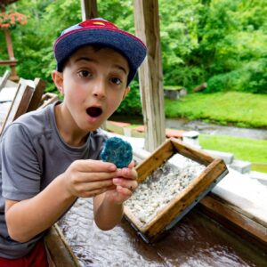 an excited kid finds a blue gemstone while sifting through earth and sand with a screen at Gem Mountain