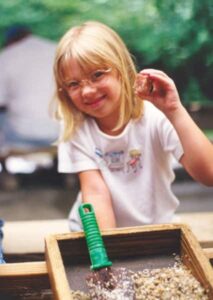 a young girl with glasses holding up a gemstone she found while flume mining