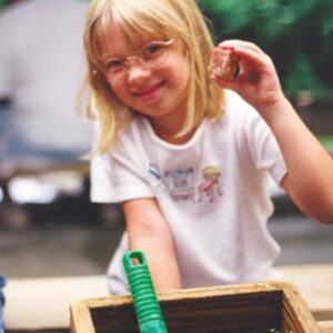 a young girl with glasses holding up a gemstone she found while flume mining
