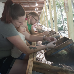 families, including a mother and young child, sift through earth and sand looking for gemstones at Gem Mountain