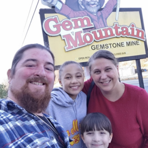 A family poses for a picture in front of the Gem Mountain sign